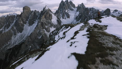 snowy cadini di misurina and hikers on a mountain ridge, dusk in dolomites, italy - reverse, drone shot