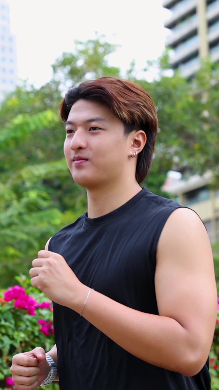 Một người đàn ông châu Á khỏe mạnh chạy bộ qua công viên thành phố trong buổi tập luyện sáng sớm đầy nắng.