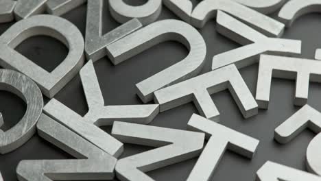 full frame close-up looped rotating background of silver metal letters on flat black surface