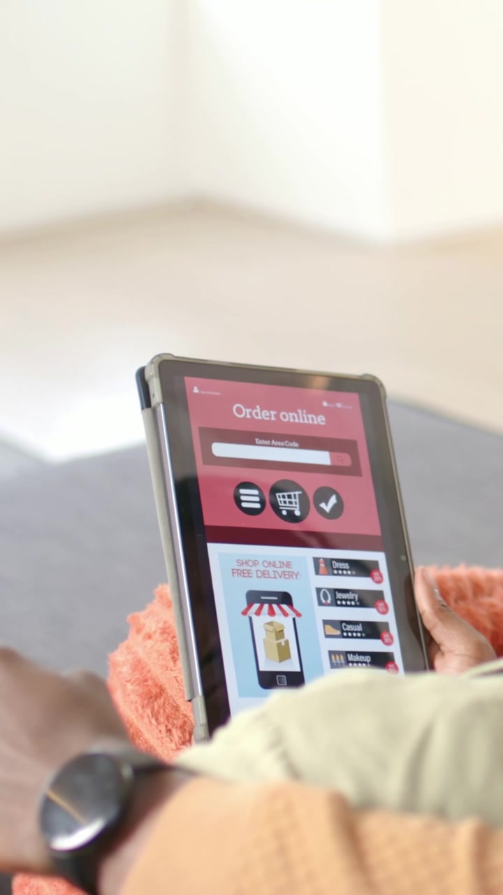 Video verticale: Uomo con maglia a maglia arancione che apre un'app per ordini, tocca il tablet per ordinare sul divano, con spazio per il testo.