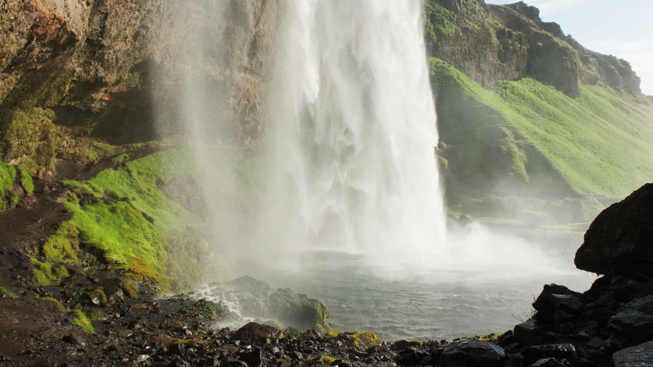 spray brumoso sobre rocas mojadas de la cascada seljalandsfoss en islandia