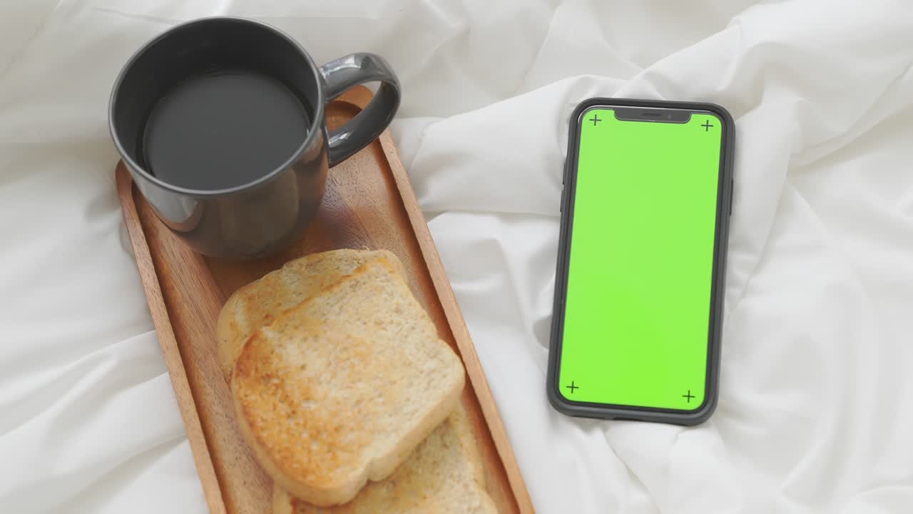 smartphone con schermo chromakey per la pubblicità. caffè e pane per la colazione in camera da letto.