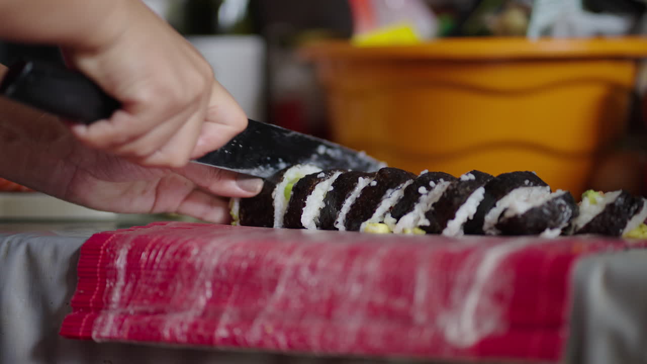 Hands carefully cut a sushi roll into neat pieces using a sharp knife in close-up view