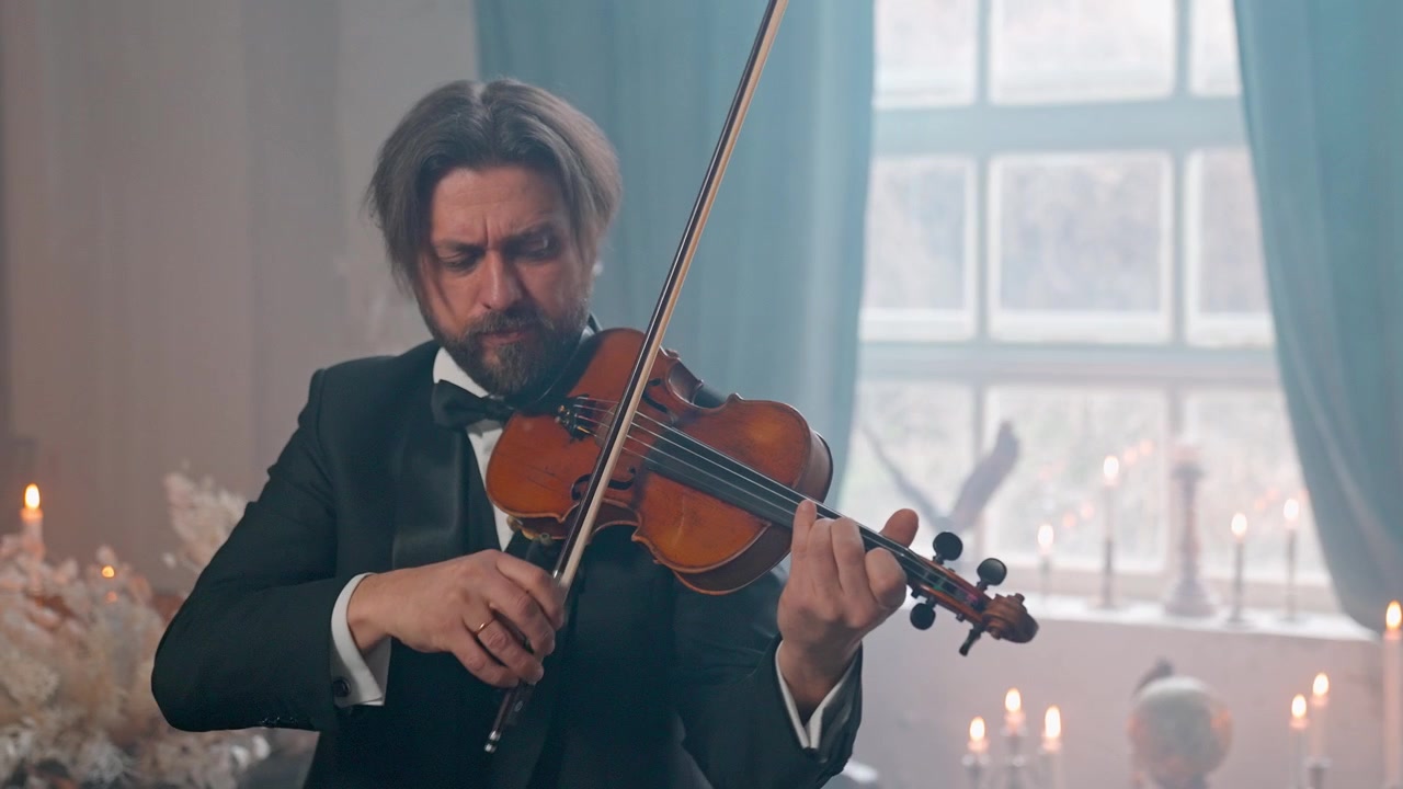 Uomo elegante in smoking che suona il violino in una stanza illuminata a lume di candela