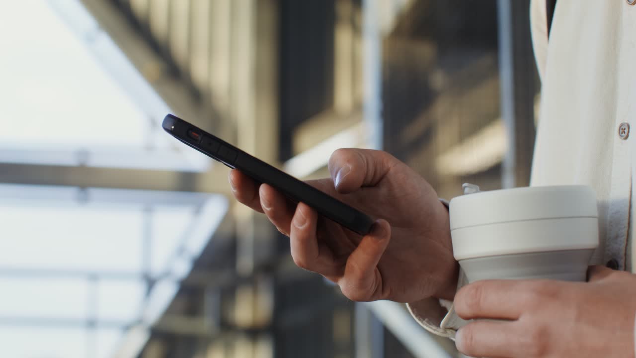 persona que usa un teléfono inteligente mientras sostiene una taza de café afuera