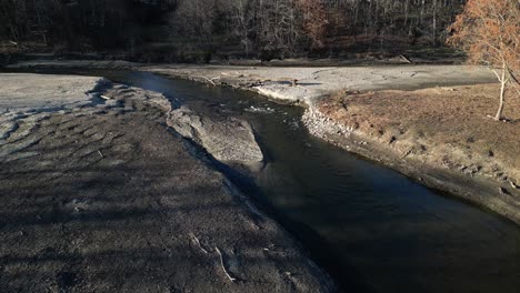 backward drone view of a pond and river flow that is badly eroded with a fallen tree