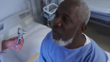 caucasian female doctor examining throat of african american senior male patient at hospital