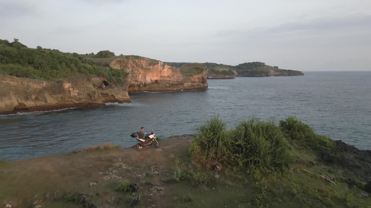 sobrevuelo aéreo: turista de motocicleta masculino disfruta de la vista en lo alto de un acantilado oceánico