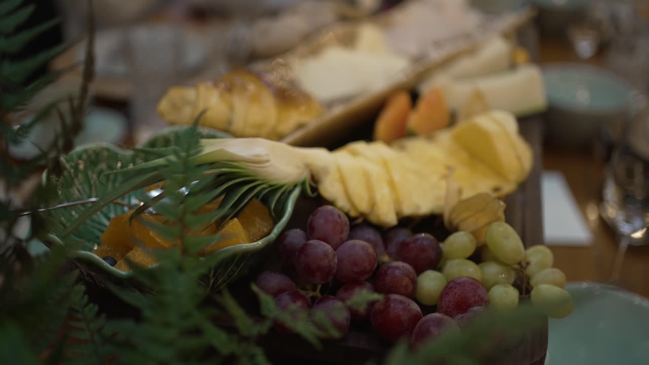 pineapple grapes cheese and sliced fruit on rustic board at elegant dining table setup