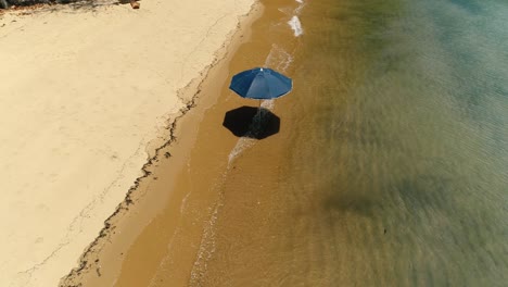Aerial-drone-orbiting-rotating-shot-of-lonely-sun-umbrella-in-the-sand-of-a-beautiful-desert-beach-in-remote-island