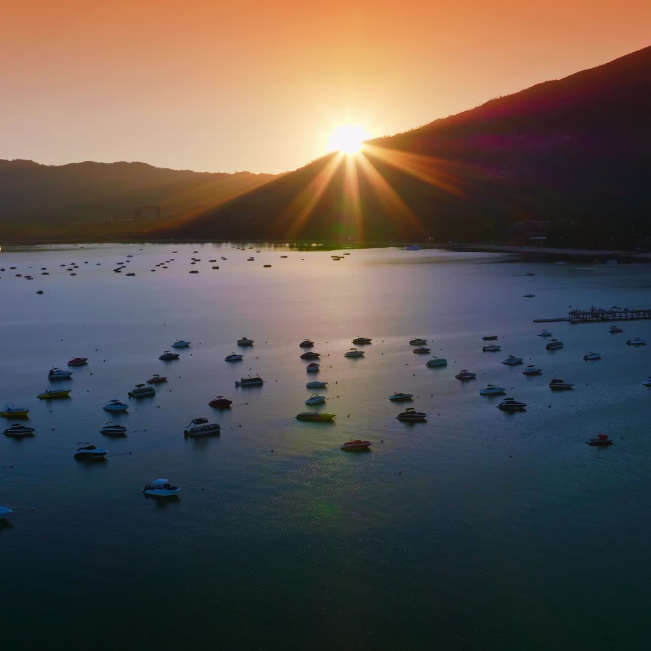 Yachts and boats holding still on the waters of Lake Tahoe, California, USA. Dark mountains silhouettes with setting sun at backdrop