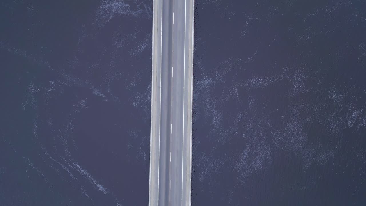 거대한 바다를 가로지르는 자동차 다리 위에서 대각선으로 비행하는 드론, 아래에서 파도가 부 ⁇ 히고