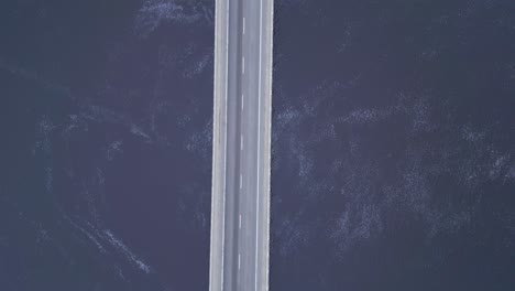 diagonal drone flight over a car bridge that spans across the vast ocean, with waves crashing below