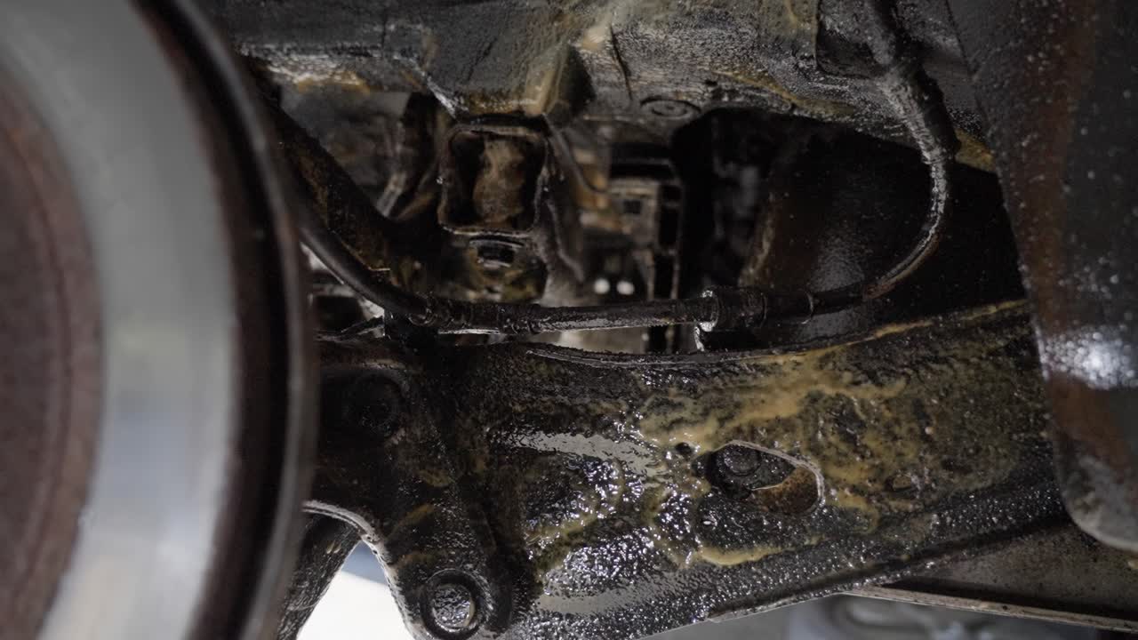Slow, handheld push in past rear brake disc showing car suspension, control arms and beams coated with lanolin rust protection product