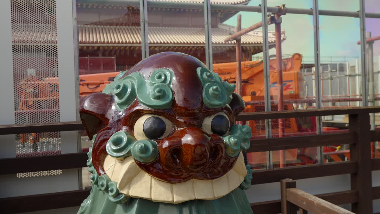 Ripresa ravvicinata orbitante di una tradizionale statua guardiana Shisa di Okinawa, posta sullo sfondo dell'impalcatura di costruzione del Castello di Shuri e degli sforzi di restauro in corso dopo i danni dell'incendio del 2019