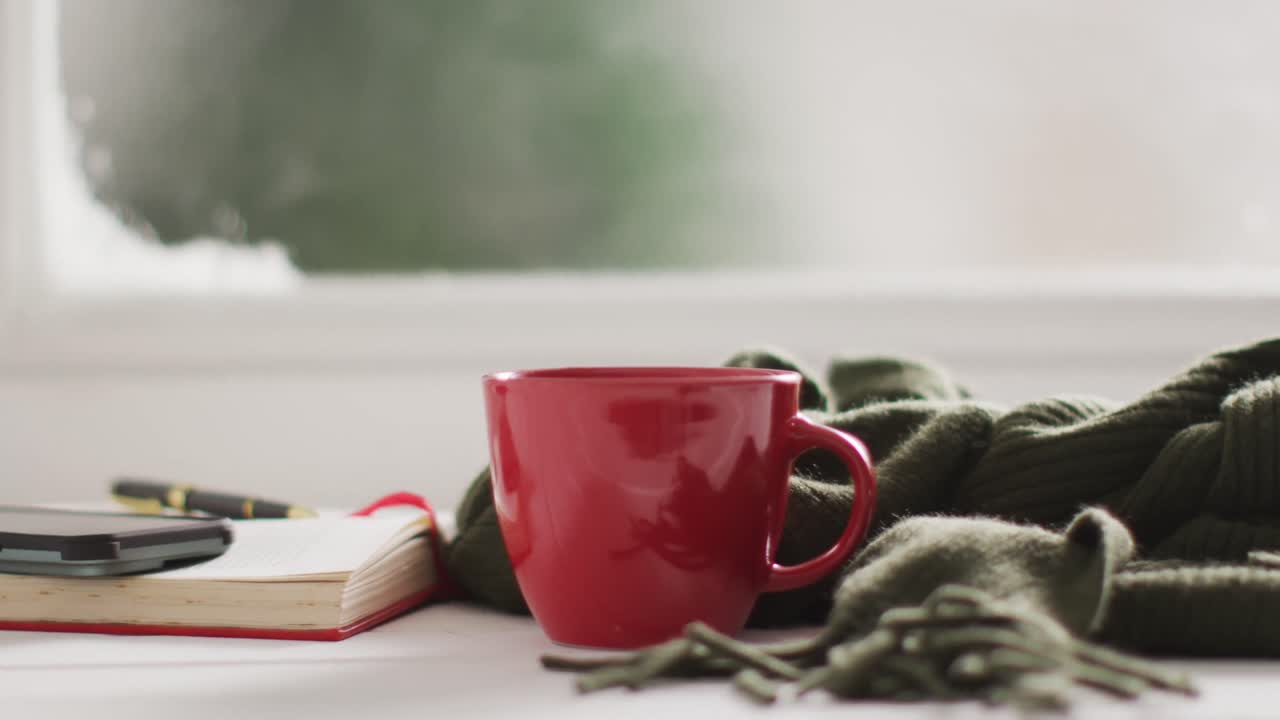 video de una taza de café caliente y un libro sobre una ventana congelada y nevada