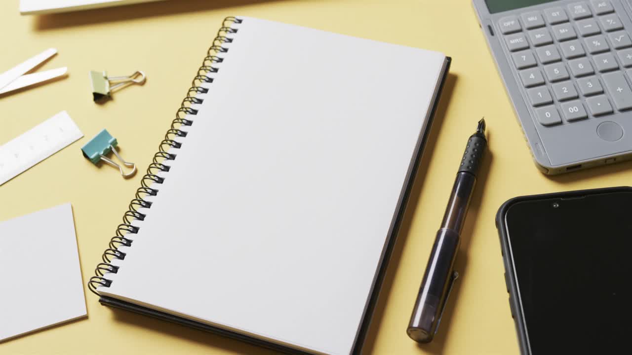 Close up of notebook, smartphone and school stationery on yellow background, in slow motion
