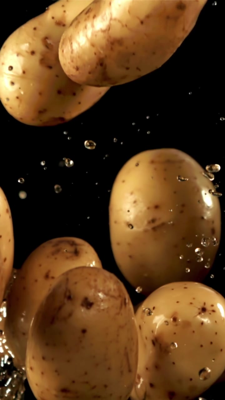 Patate fresche che cadono con schizzi d'acqua su sfondo nero