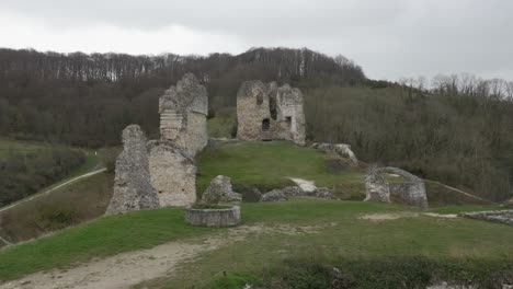 Decrepit-relic-ruins-of-old-concrete-rock-structures-on-grassy-hillside-at-forest-edge