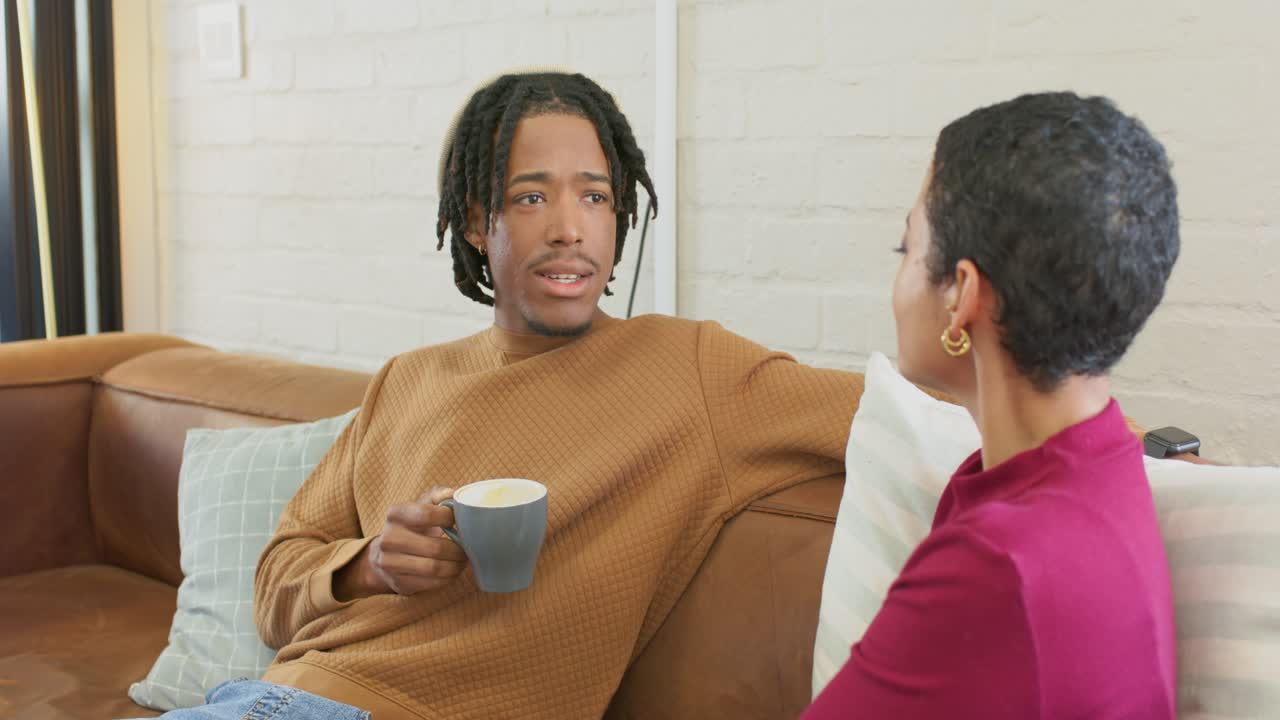 Diverse couple starting conversation with man shifting gaze and sipping coffee mug in living room