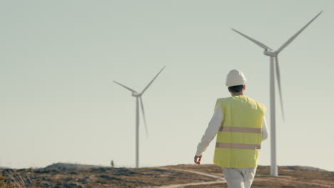 plano general de un ingeniero de energía renovable caminando y revisando turbinas eólicas, simbolizando la importancia de la energía sostenible para el futuro de nuestro planeta