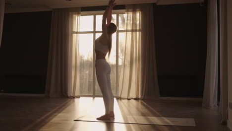 lens flare :a young woman in white sportswear is stretching with a large hall with large windows in a slow-motion scheme the sun's rays shine through the window. healthy lifestyle healthy morning