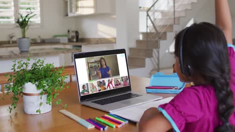 Schoolgirl-using-laptop-for-online-lesson-at-home,-with-diverse-teacher-and-class-on-screen