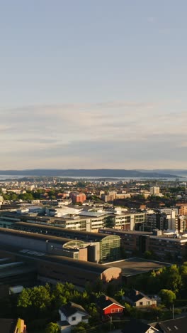 a vertical drone shot captures the entirety of oslo, its charming blend of urban life and green spaces framed by the expansive blue of the sky and the glistening sea in the background.