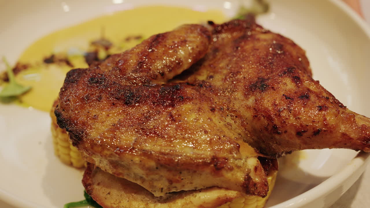 Primo piano di una coscia di pollo alla griglia servita con salsa cremosa, mais e verdure.