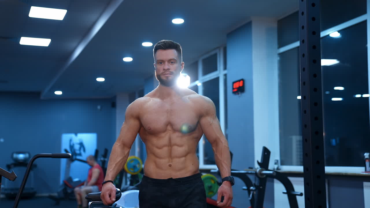 Half length portrait of shirtless sportsman. Muscular bodybuilder with naked torso in the gym. Handsome man with perfect athletic body moving to camera.
