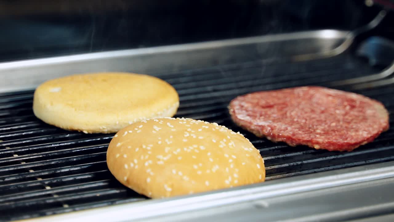 Making tasty hamburger dish. Halves of bun and meat cutlet for burger on hot grill pan. Preparing fast food. Cooking food in professional restaurant kitchen