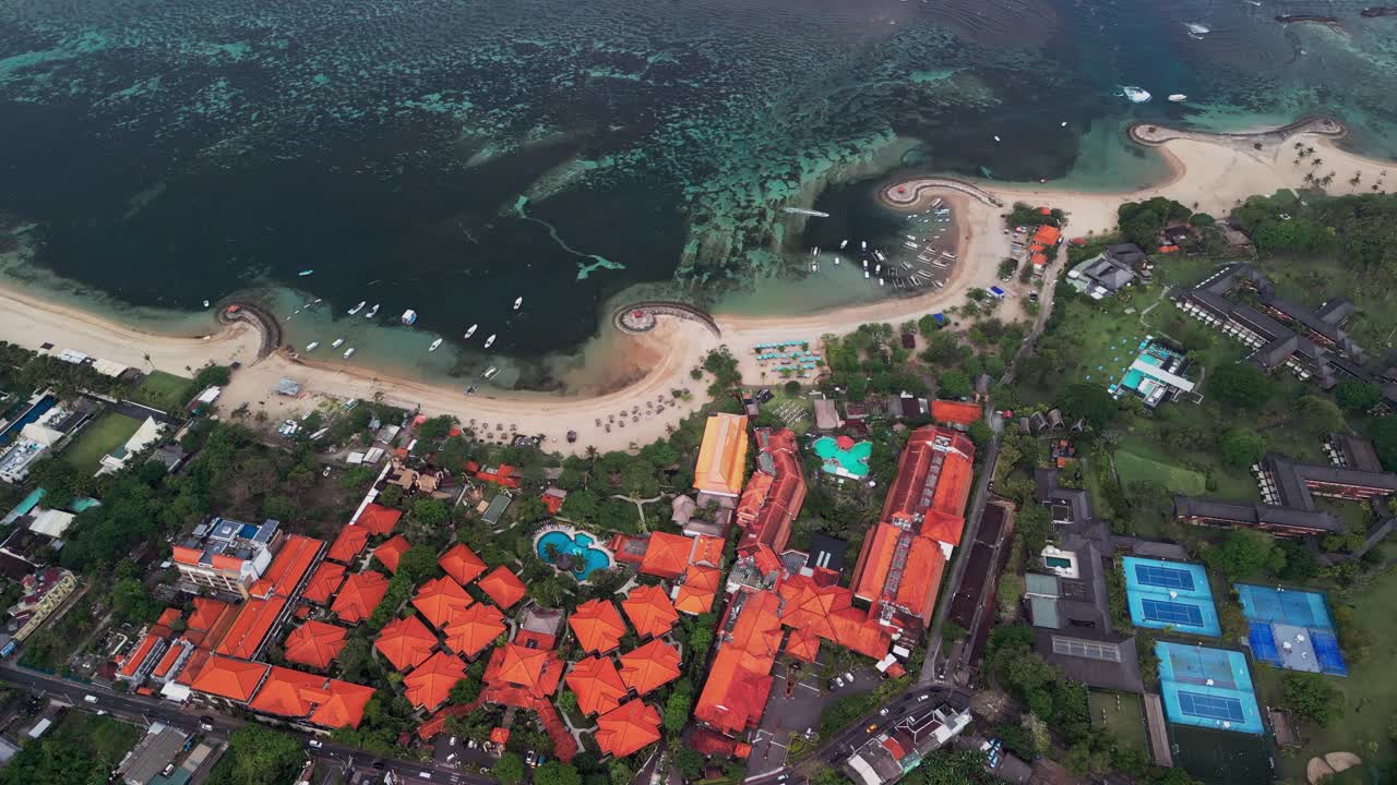 Aerial drone video of Bali Island showcasing sandy beaches, vibrant ocean reefs, and colorful resorts. The tropical coastline captures the unique balance of natural beauty and local architecture