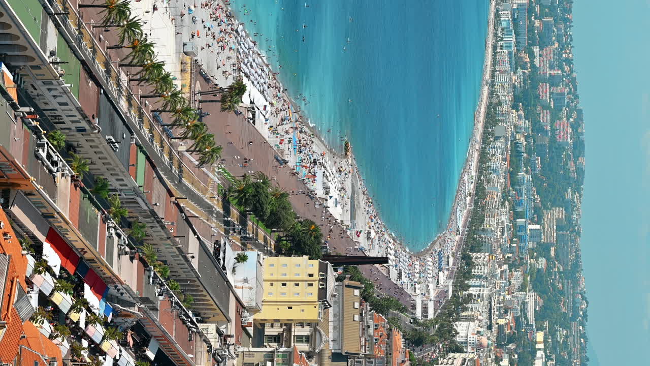 View of the cote d'Azur in Nice, France. Multiple resting on the beach people, buildings, blue water of the Mediterranean sea