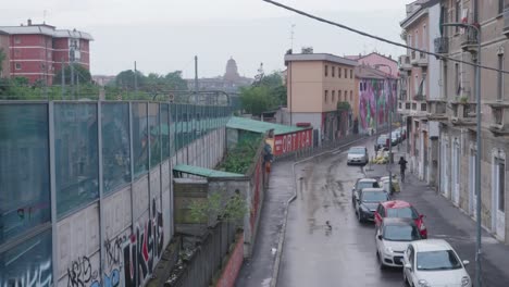 Suburb-street-with-graffiti,-people-and-cars-parked-in-Milan,-view-from-above