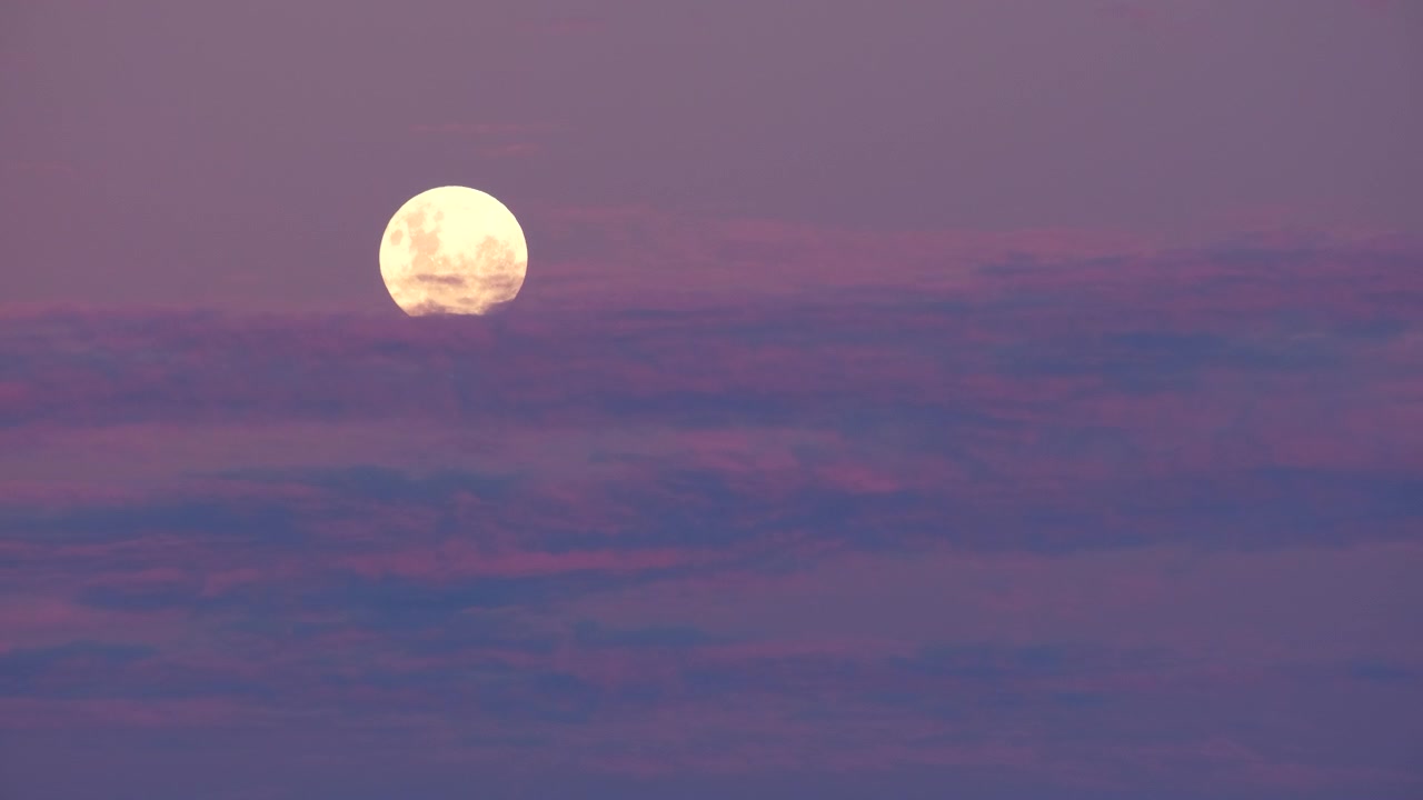 Lua cheia redonda atrás de nuvens roxas e rosas no céu crepuscular.