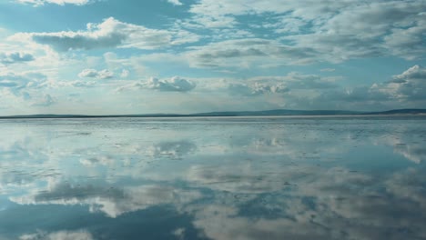 Niedrige-Luftaufnahme-Des-Salzsees,-Die-Den-Blauen-Himmel-Und-Die-Wolken-Widerspiegelt