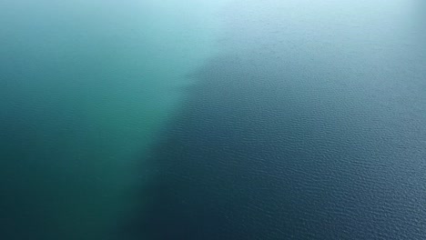 drone flight over a brilliant blue lake with different shades of blue and wind that creates waves on the surface of the water