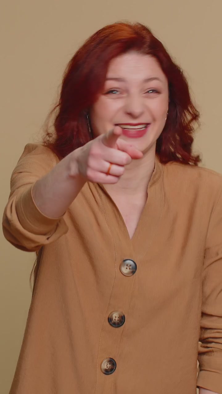 Sorridente sorridente donna dai capelli rossi che indica con il dito la telecamera ridendo ad alta voce aneddoto divertente