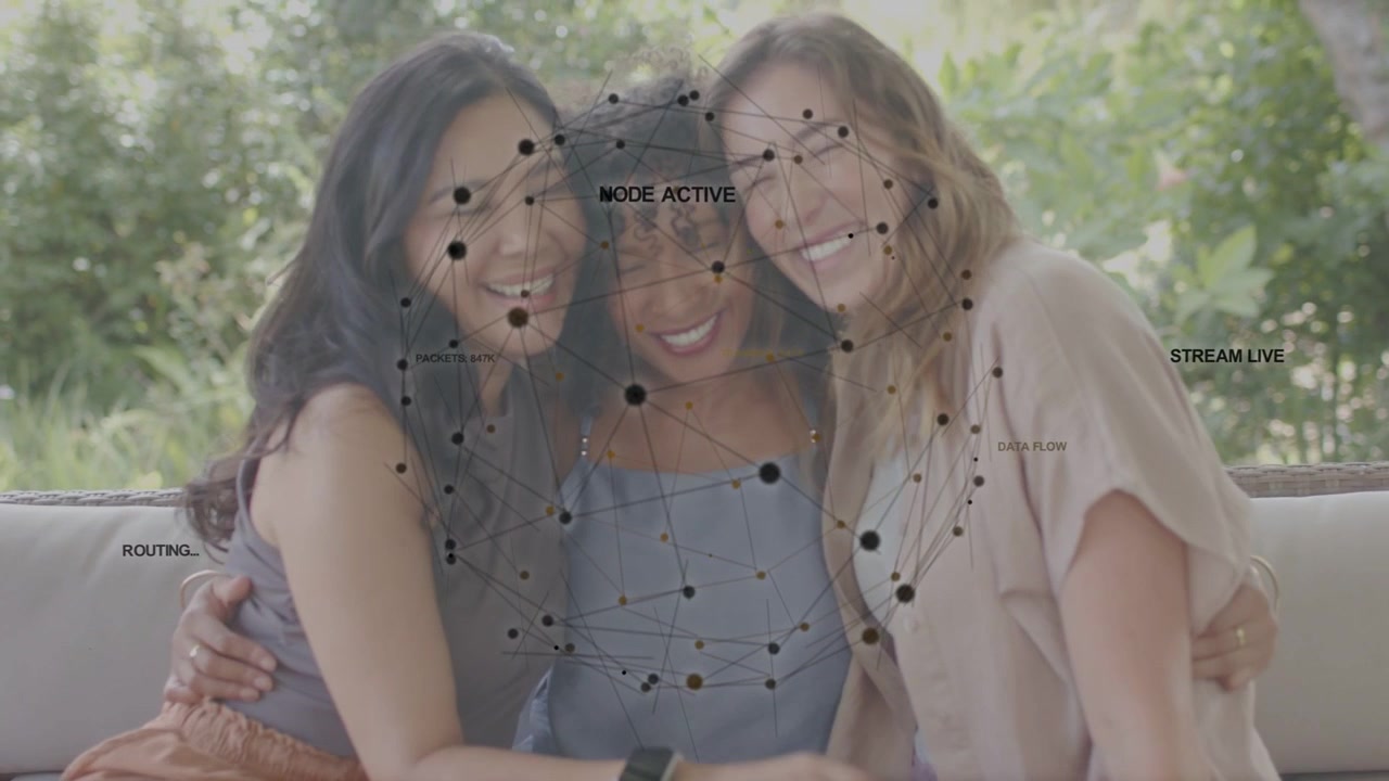 La telecamera si allontana, tre donne che ridono e si abbracciano sul divano, con una sovrapposizione di rete che traccia una demo tecnologica.