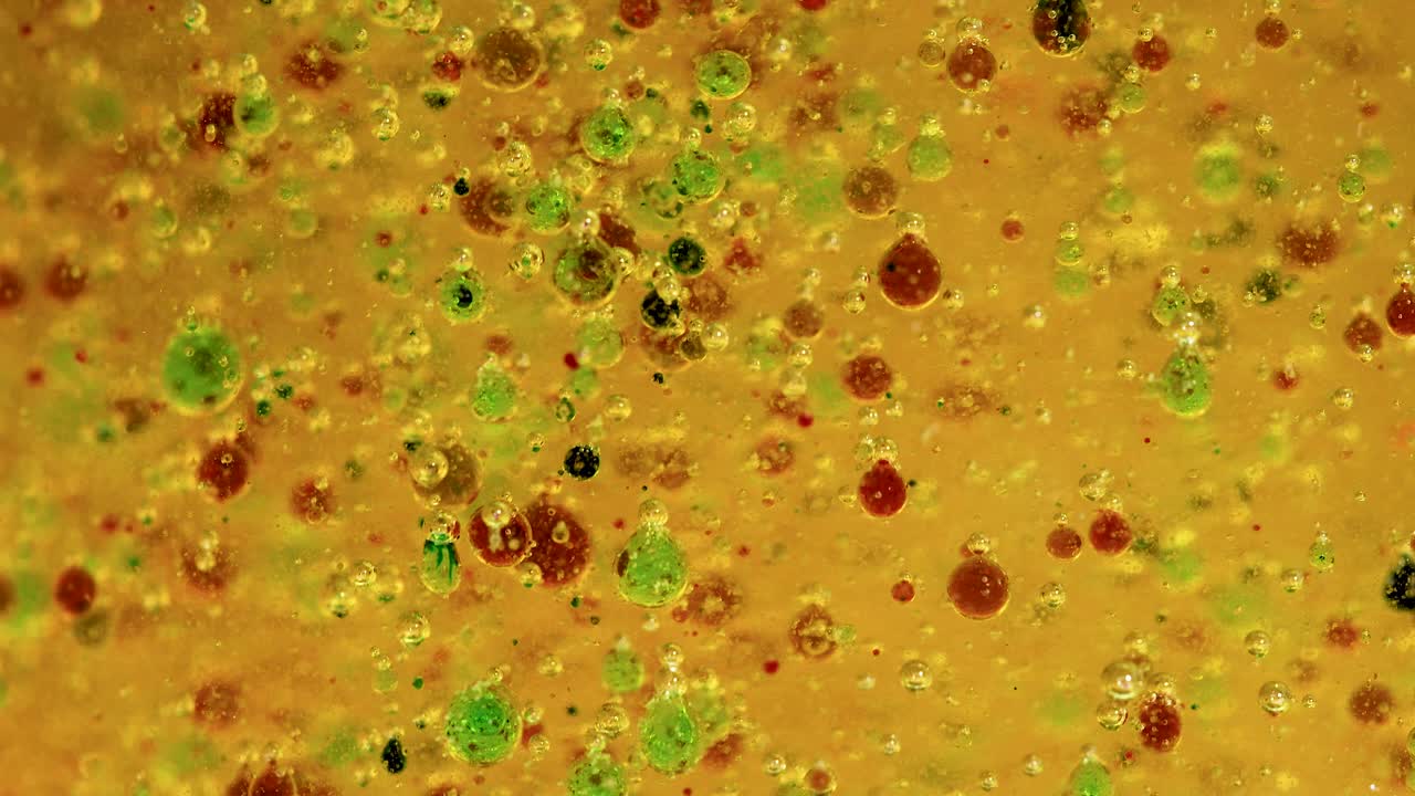 gotas vibrantes de verde y rojo interactúan dinámicamente en un líquido amarillo, mostrando una reacción química hipnotizante