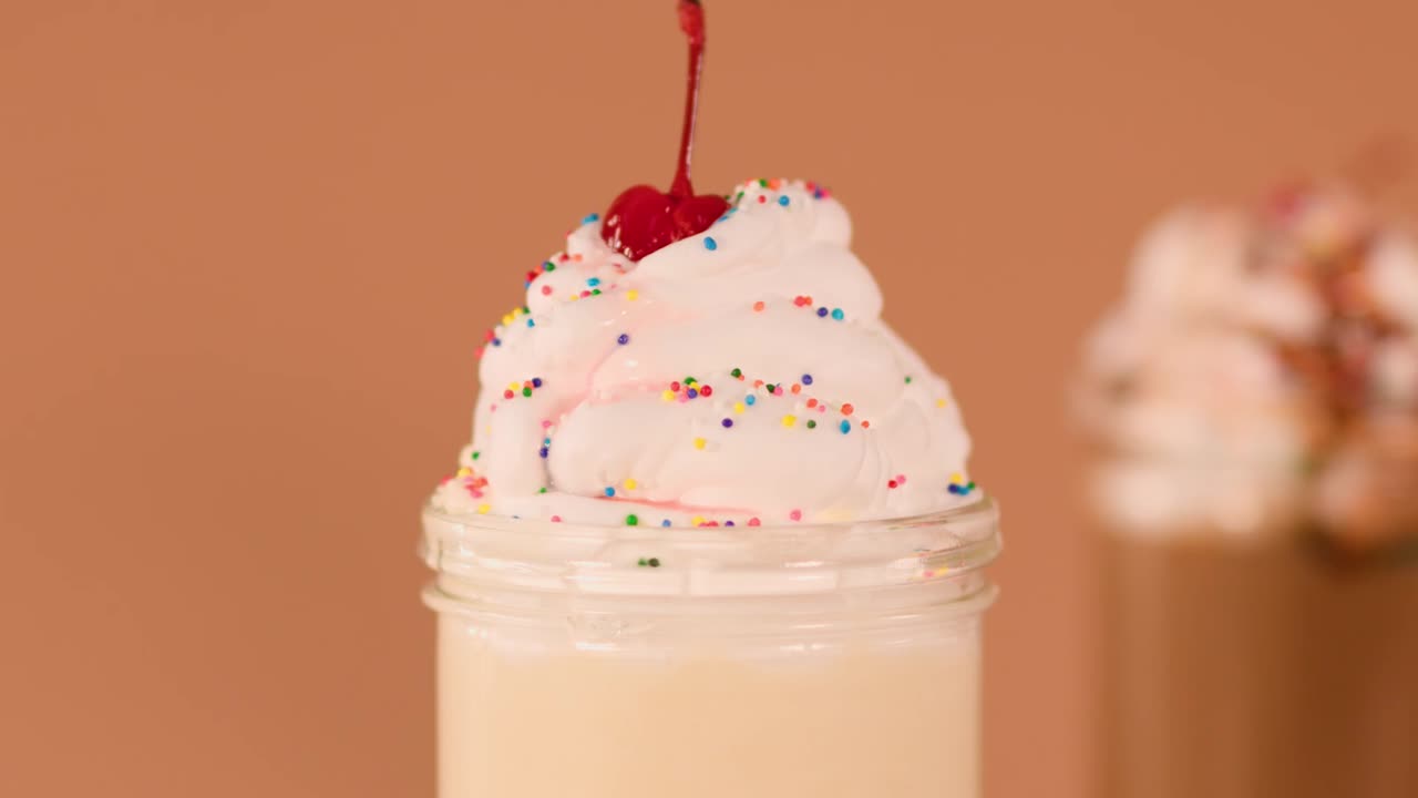Close-up of a hand placing a red striped straw into a creamy vanilla milkshake topping