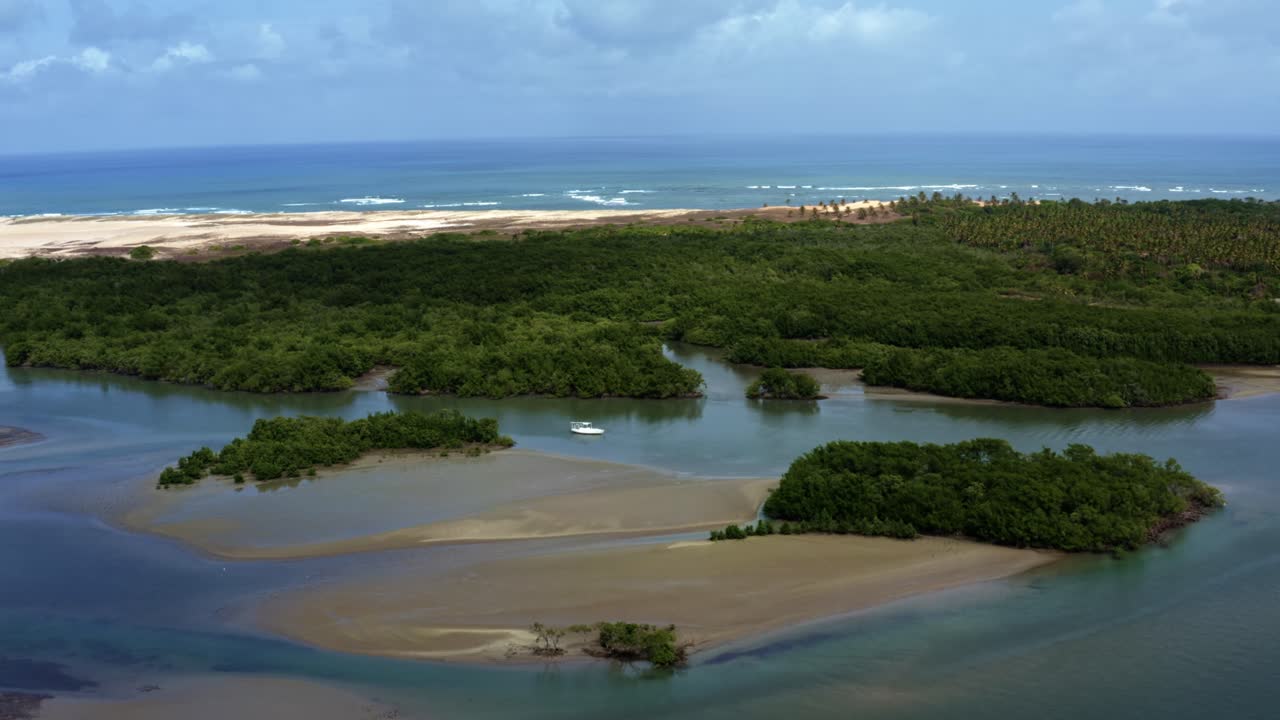 Left trucking aerial drone shot of a boat anchored in the Guara&iacute;ras Lagoon during low tide with sand banks and patches of mangroves with the Muqui&ccedil;o Beach in the background in Tibau do Sul, Brazil