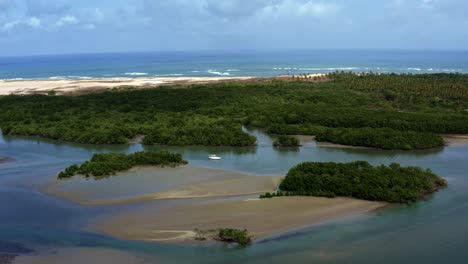 left trucking aerial drone shot of a boat anchored in the guaraíras lagoon during low tide with sand banks and patches of mangroves with the muquiço beach in the background in tibau do sul, brazil