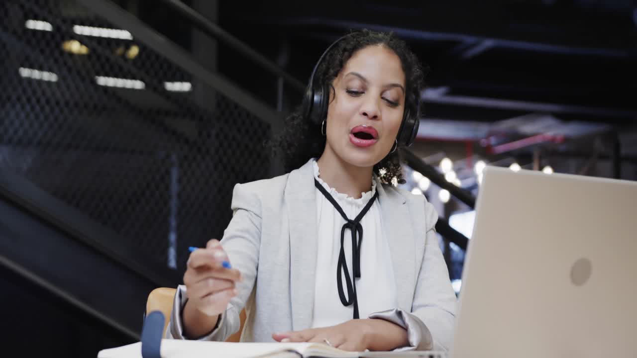 feliz mujer de negocios casual biracial haciendo una videollamada usando una computadora portátil en el salón de la oficina, cámara lenta