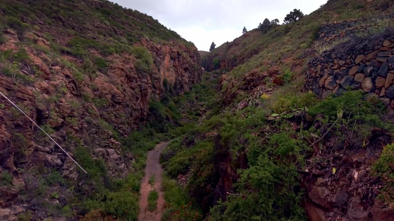 Sendero de tierra serpentea a través de un escarpado barranco volcánico con terrazas de piedra y laderas verdes