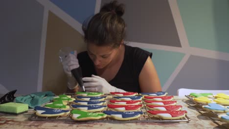 Woman-decorates-homemade-vehicle-shaped-cookies-with-sugar-icing-using-a-pastry-bag,-slide-medium-shot-4K