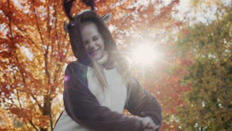 a child in a deer costume dances a cheerful dance against the backdrop of a beautiful tree with yellow leaves. the sun illuminates the girl from behind