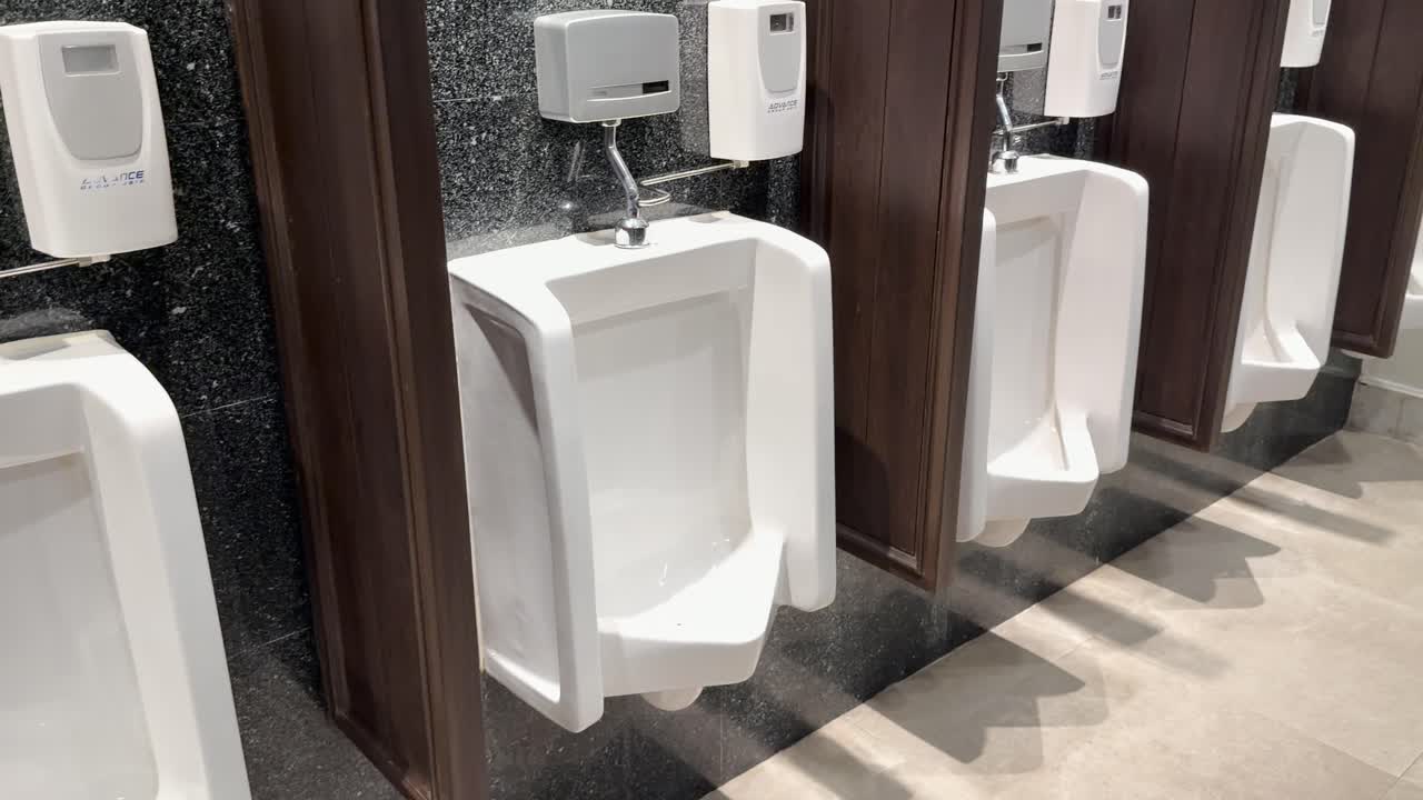 Camera pans across bright, contemporary hotel men's restroom with white urinals and granite partitions