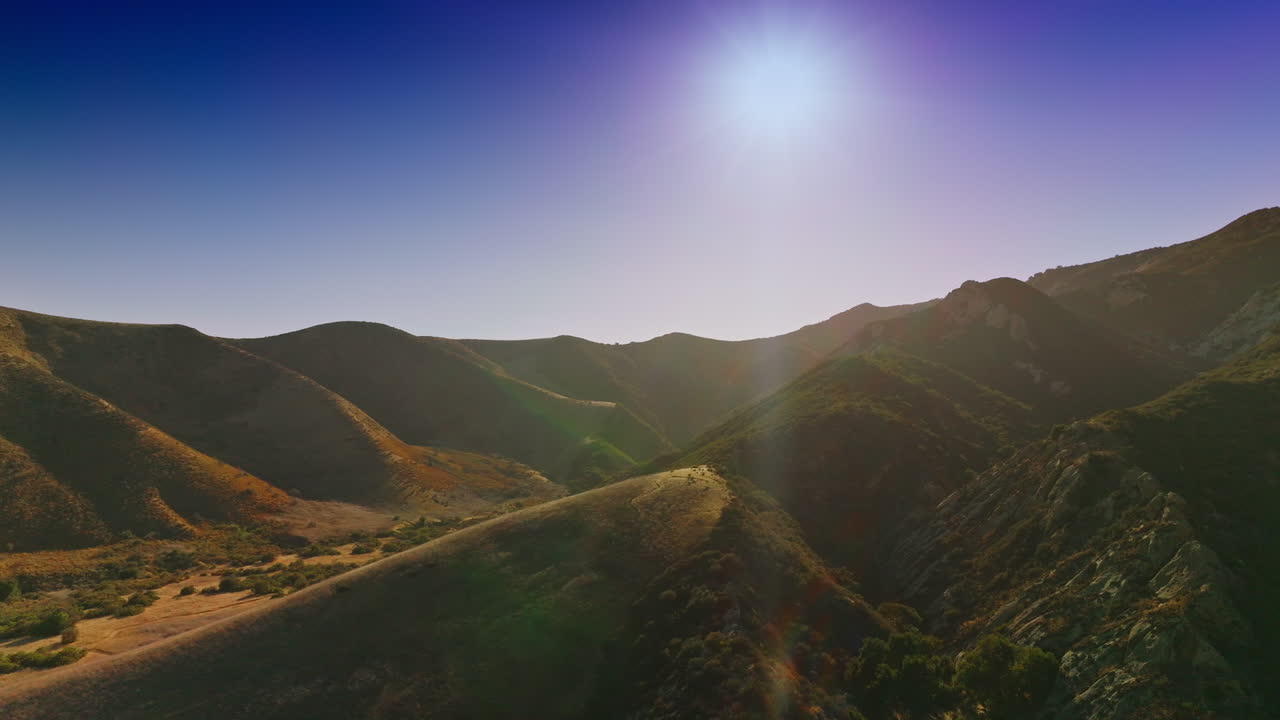 Amazing mountainous territory with no trees growing on. Drone rising over the mountains in the rays of bright sun.