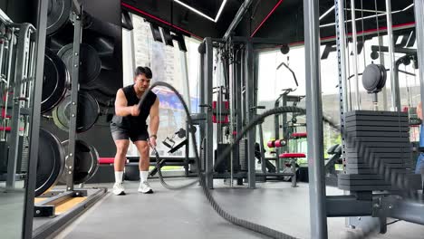 a person performs a vigorous battle rope exercise in a well-equipped gym with bright lighting and dynamic camera angles